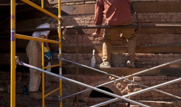 People sitting of scaffolding working on a structure made of bricks.