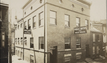 Black and white photo of a building with a sign: Public Baths and Wash House
