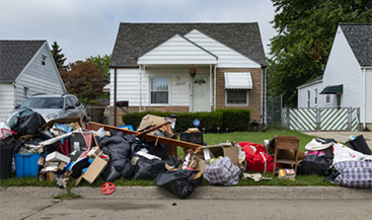 Piles of trash and furniture left on the curb in front of a small house
