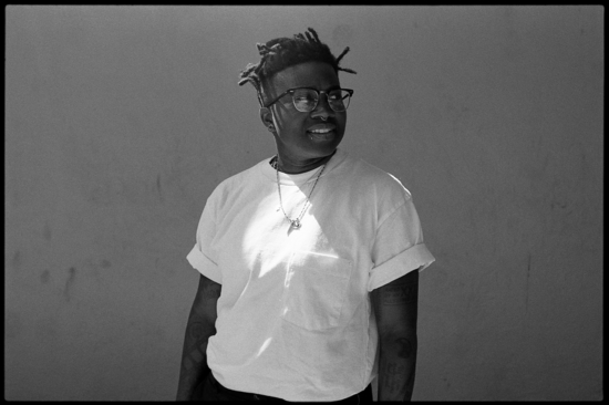 black and white film image of McClodden wearing contrasting bright white shirt against dark grey background, looking off camera