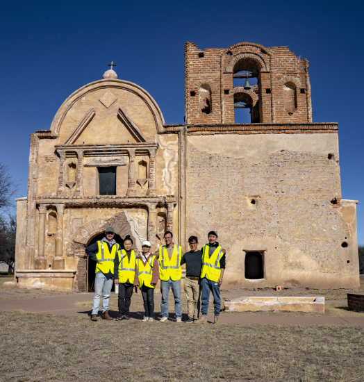 Photograph of several people standing in front of an old stone church