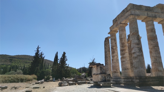 Sanctuary of Zeus at Ancient Nemea, view capturing the impression of the Temple of Zeus and sacred grove relation in ancient time. At the foreground is the restored temple’s east facade with ramp access and the remains of the long altar, at the background vegetation that includes cypress trees. The position of the trees that are seen today is not exactly that of antiquity, photo by Antonios Thodis. «The copyright of the depicted monuments belongs to the Hellenic Ministry of Culture and Sports (ν.3028/2002)»
