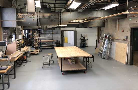 Unoccupied studio space with table in center and supplies and smaller work tables on the sides.