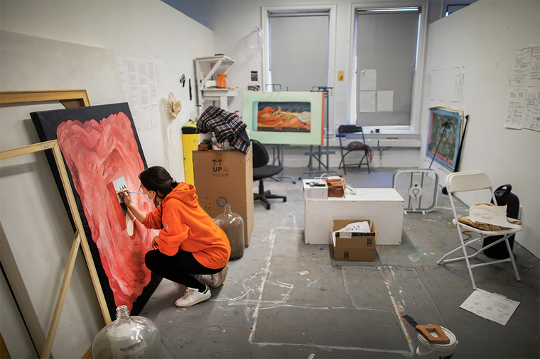 Woman painting on canvas in orange hoodie and blue jeans