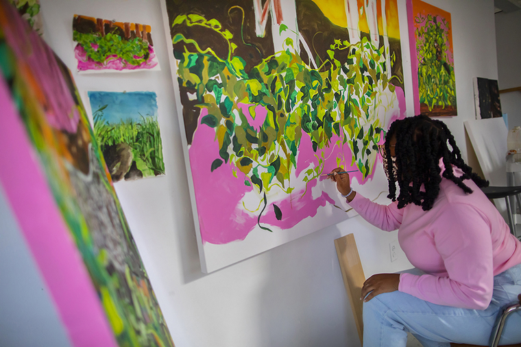 Patricia Renee Thomas works on a neon-palette landscape painting mounted to the wall.