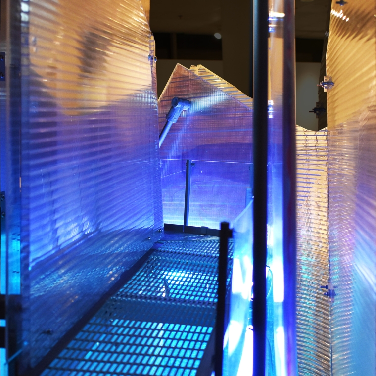 A glowing corridor of light and material contrast, this image captures a key moment from Iridescent Offset, where translucent polycarbonate panels, perforated steel flooring, and internal LED lighting create an immersive spatial experience. The layered construction explores offset geometries and visual distortion, inviting viewers to navigate shifting perceptions of depth, reflection, and transparency.