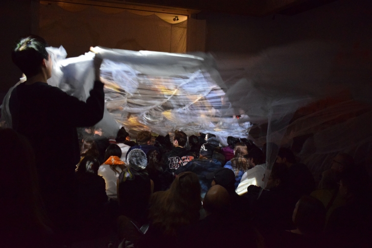Photo from the final immersive, interactive multimedia performance where four performers extend a long fabric over the audience to symbolize flooding.