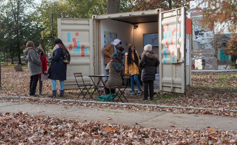 Students holding an information booth in a small cargo container during fall