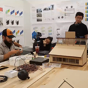 Three students sit at a table with archectural models