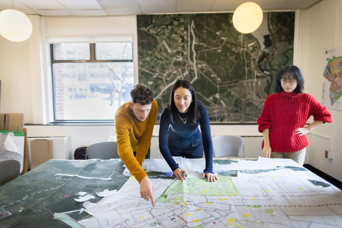 Three students gesture towards a map 