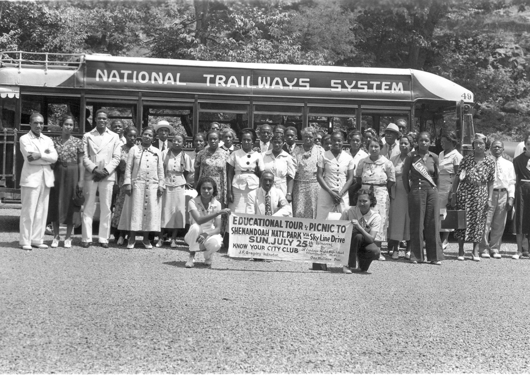 A group of people pose in front of a tour bus in an old b&w photo