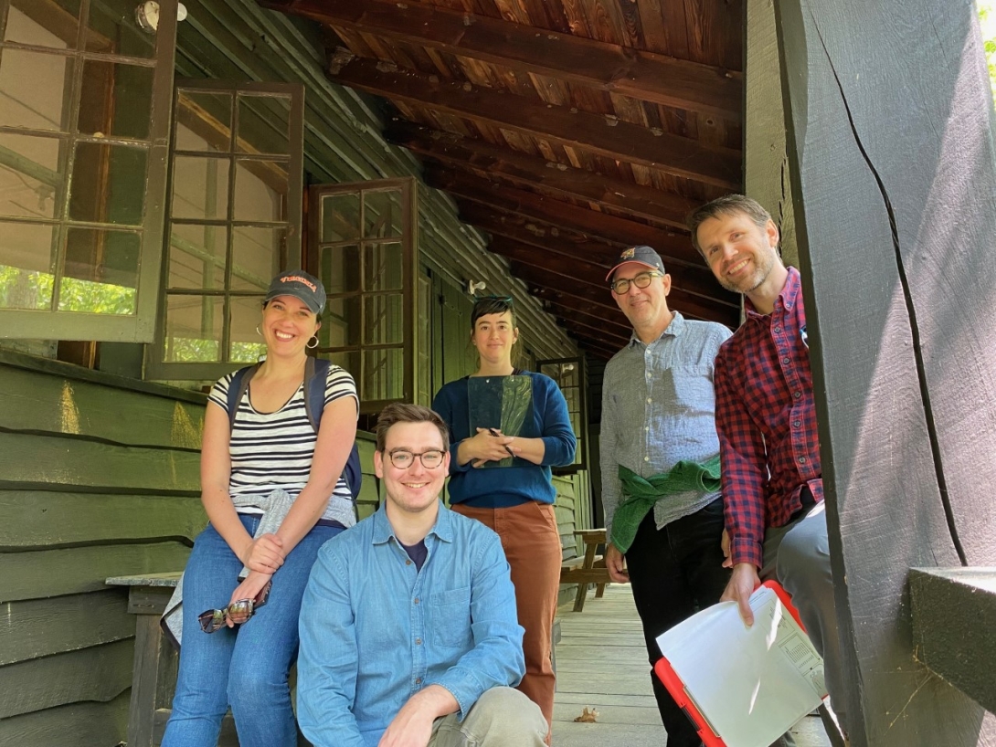 A group of five people pose on the porch of a cabin
