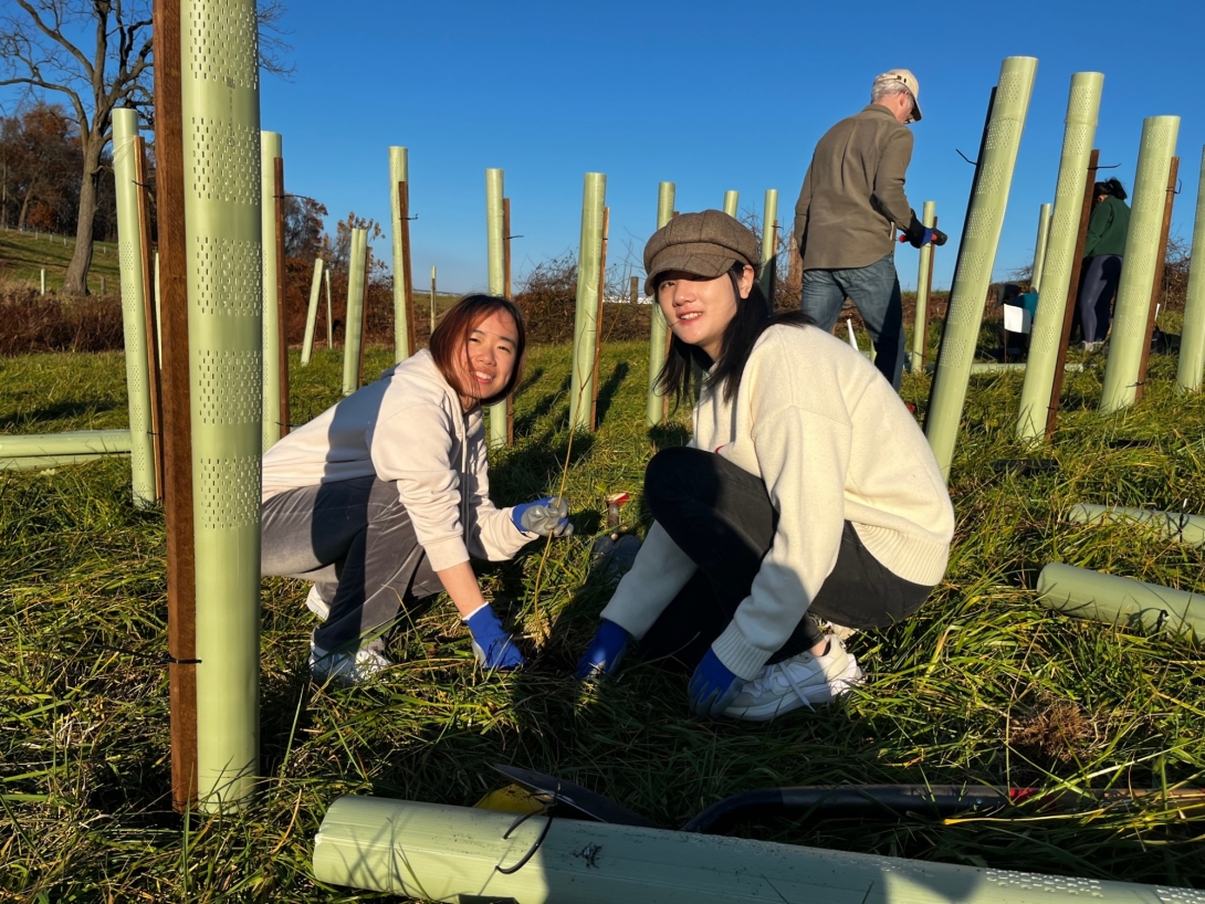 Two young Asian women next to saplings in a field