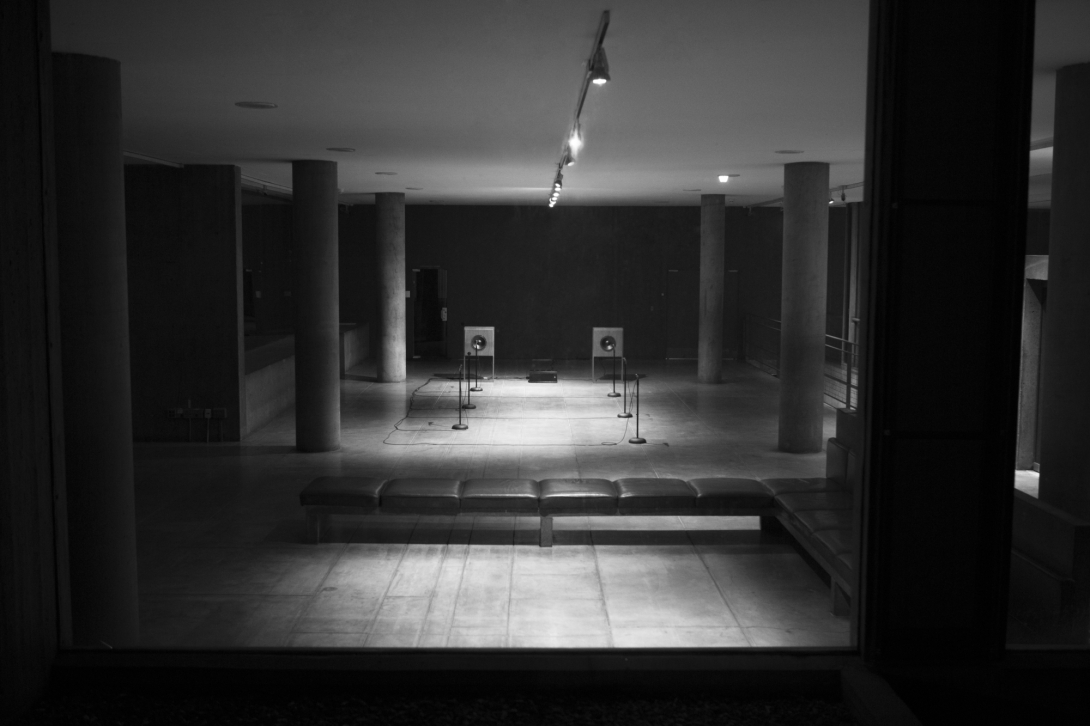 B&W photo of empty hall with mics on stands
