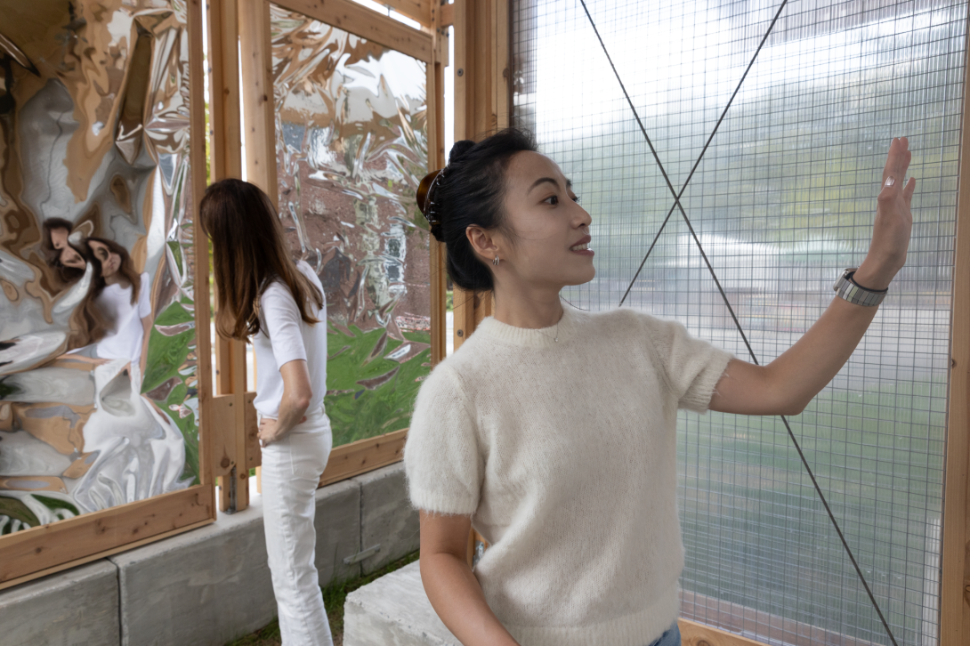 Two women inside pavilion gesture towards reflective and translucent panels
