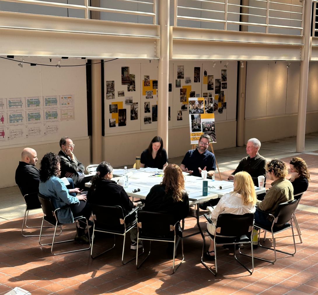 Group of people at oval conference table with architectural drawings in atrium