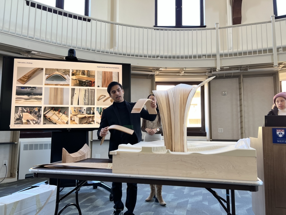 Student stands with wood model on table in front of screen