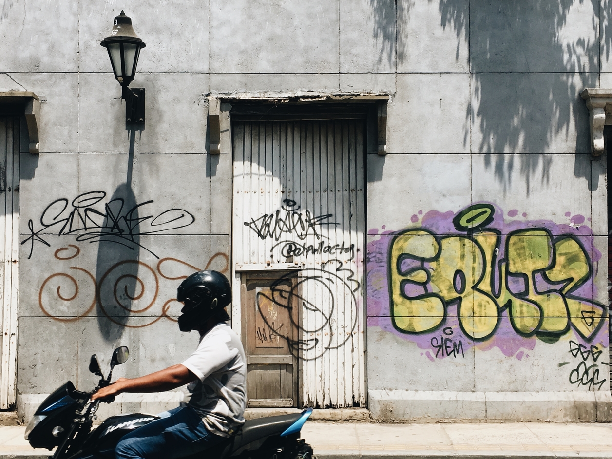 Man riding a motorcycle past a building with graffiti