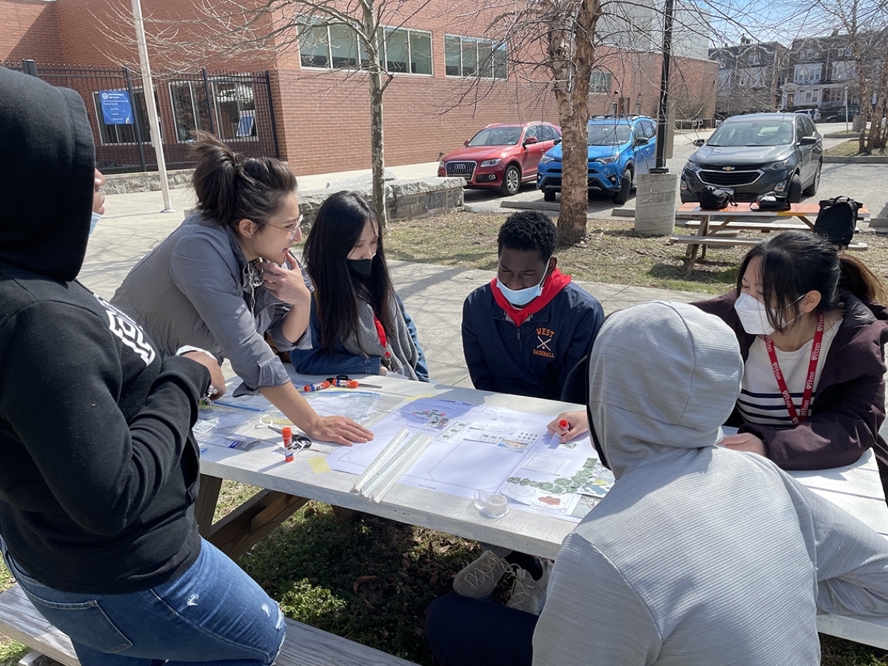 A group of people looking at drawings while sitting at a picnic table