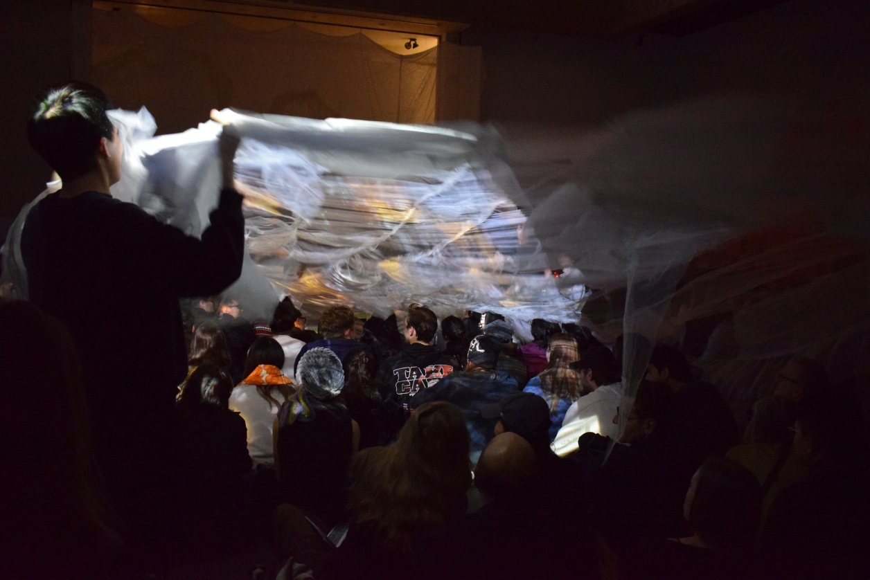 Photo from the final immersive, interactive multimedia performance where four performers extend a long fabric over the audience to symbolize flooding.